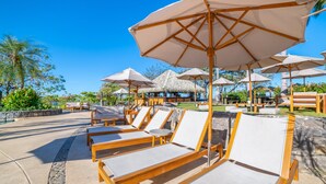 Un espace aménagé au bord de la piscine, avec des chaises longues et des parasols, entouré de murs en pierre et de plantes tropicales.