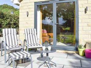 A patio with two striped lounge chairs, a small round table, and a glass door leading to an outdoor area. - 1 bedroom accommodation in Wingerworth (Wingerworth)