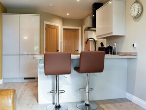 A modern kitchen with two bar stools, a wooden door, and a clock on the wall. - 1 bedroom accommodation in Wingerworth (Wingerworth)