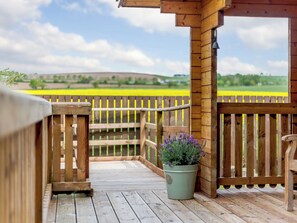 A wooden deck with a view of a yellow field, a wooden fence, and a potted plant with purple flowers.