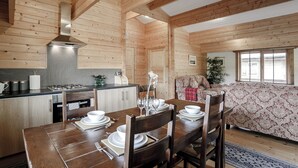 Un interior de madera con una mesa de comedor para cuatro personas, una zona de cocina y un sofá estampado.