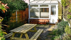 Een huis met een terras, een houten tafel en een tuin.