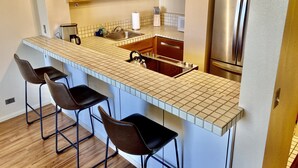 Une cuisine moderne dotée d’un îlot central, de tabourets de bar, d’appareils électroménagers en acier inoxydable et d’armoires en bois.