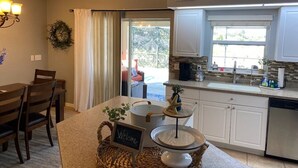 A modern kitchen with white cabinets, a dining area with wooden chairs, and a view through a glass door to an outdoor patio. - Oasis home in SW Florida - Heated in-ground pool on a fresh water canal! (Cape Coral)