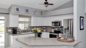 A modern kitchen with white cabinets, a granite countertop, a central island, and a ceiling fan. - Oasis home in SW Florida - Heated in-ground pool on a fresh water canal! (Cape Coral)