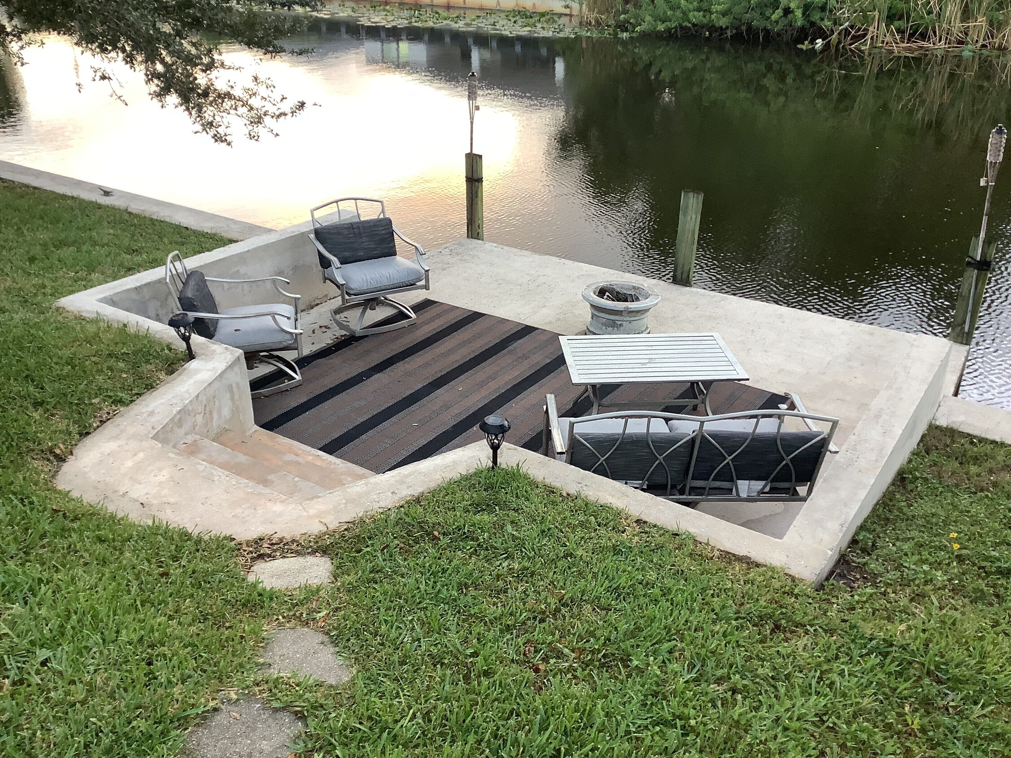 Un patio de concreto con alfombra a rayas, dos sillas, una mesa y un brasero.