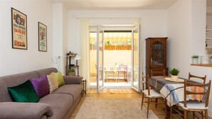 A living room with a sofa, a dining table with chairs, a cabinet, and a sliding glass door leading to an outdoor area with plants.