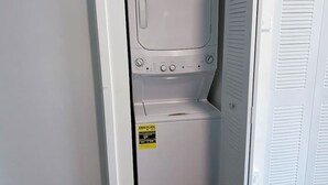 Uma lavanderia compacta e branca com máquina de lavar e secadora frontais, painel de controle e porta com venezianas.