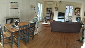 A living room with a wooden floor, a sofa, a dining table with chairs, and a TV. - 3-bedroom apartment in the heart of a medieval village in Vallespir (Pyrenees). (Arles sur Tech)