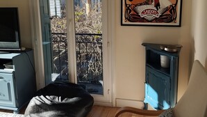 A living room with a large window, a chair, a bean bag, a small cabinet, and a framed artwork on the wall. - 3-bedroom apartment in the heart of a medieval village in Vallespir (Pyrenees). (Arles sur Tech)