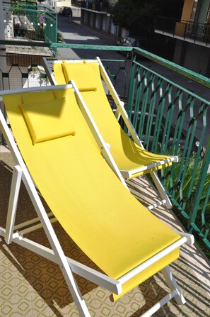 Two yellow sun loungers on a balcony with a green railing, overlooking a street.