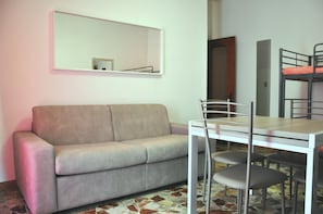 A room with a sofa, a dining table with chairs, a bunk bed, and a mirror on the wall. - VIALE REPUBBLICA 329 1 (Pietra Ligure)