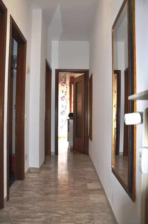 A hallway with wooden doors, a tiled floor, and a mirror on the right wall.
