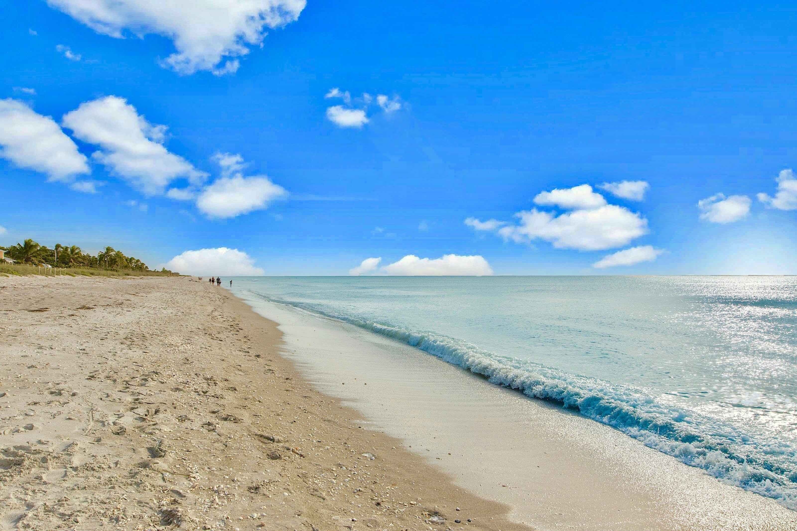Une plage avec une eau d’un bleu limpide, un rivage sablonneux et quelques personnes au loin.