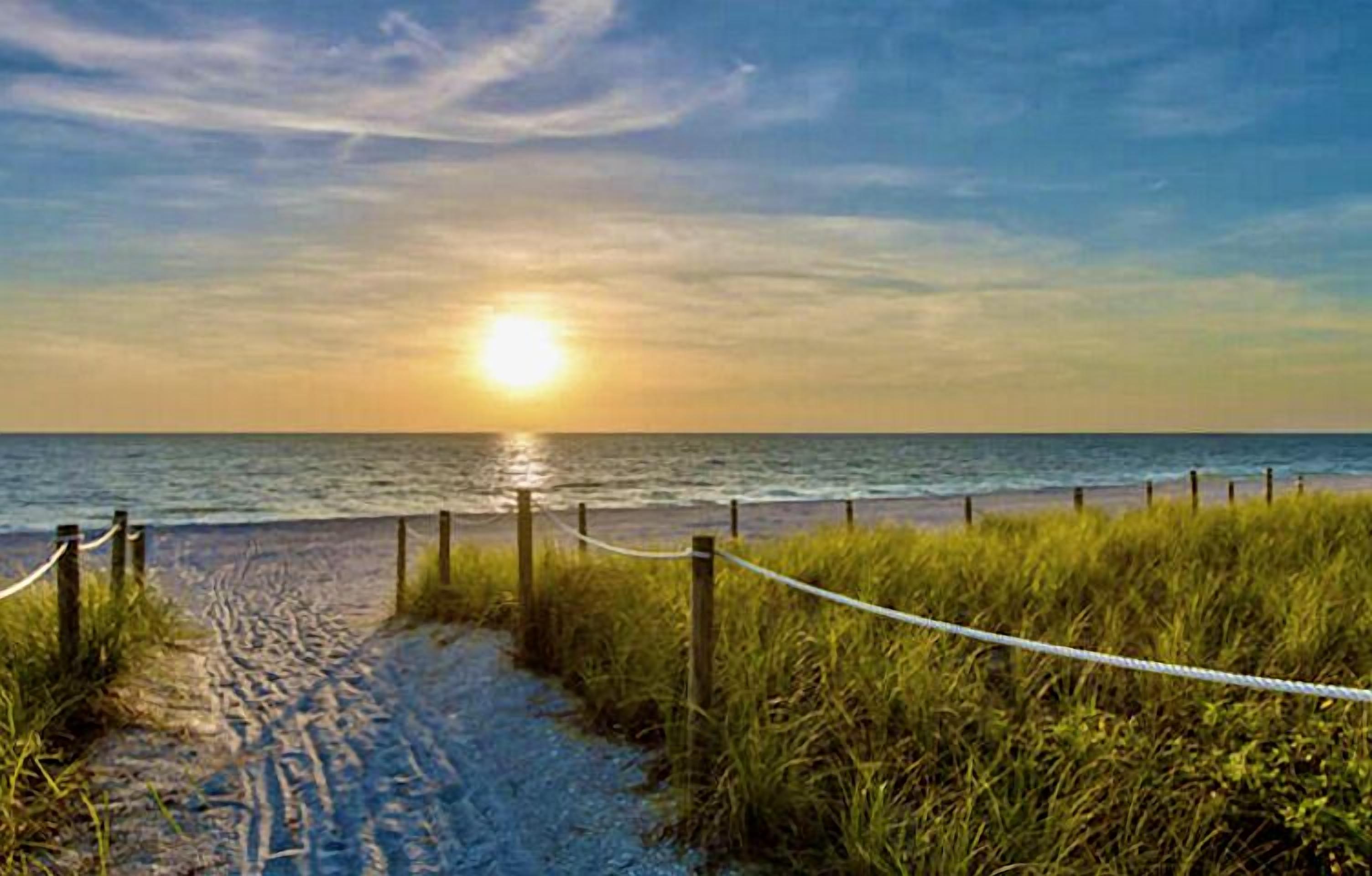 A beach path leading to the ocean with a rope barrier and wooden posts.