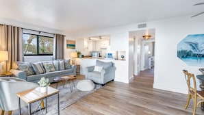 A modern living room with a sofa, armchairs, a coffee table, and a dining area with a chair. A kitchen is visible in the background. - Stunning Views Casual Lux Décor - Directly on the Beach Jensen's “On the Gulf” North Beach 2 (Captiva)