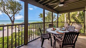 A covered outdoor dining area with a view of the ocean and palm trees. - Stunning Views Casual Lux Décor - Directly on the Beach Jensen's “On the Gulf” North Beach 2 (Captiva)