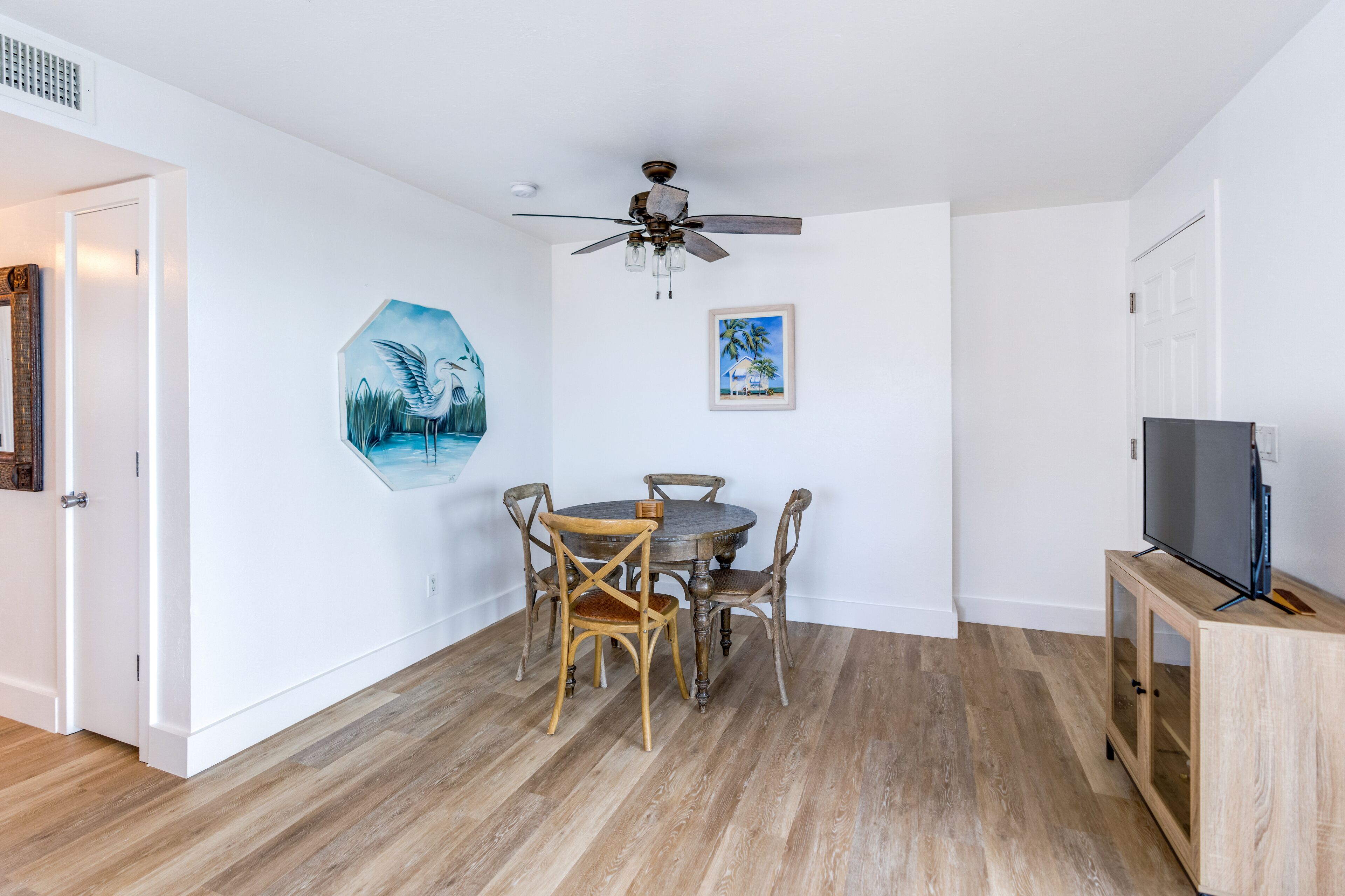A dining area with a round wooden table and four chairs, a ceiling fan, and a television on a wooden cabinet.