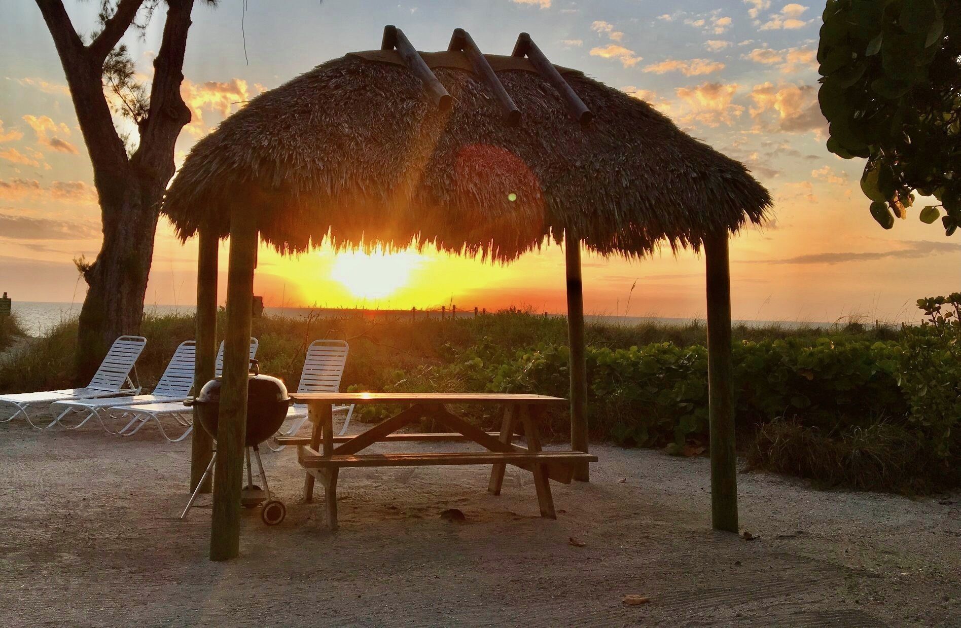 A beach scene with a thatched-roof gazebo, two lounge chairs, and a picnic table.