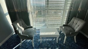 Ein Zimmer mit zwei Ledersesseln, einem weißen Couchtisch und einem großen Fenster mit Jalousien.