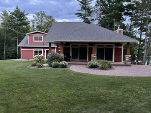 A two-story house with a covered patio, a brick driveway, and a well-maintained lawn. - Modern Lake House with Stunning Views (Medford)