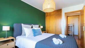 Un lit bien fait, avec une couvre-lit bleue et du linge de lit blanc, deux lampes de chevet et une armoire en bois.