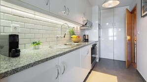 Une cuisine moderne avec des meubles blancs, un plan de travail en granit, un évier encastré et une machine à café.