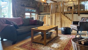 A cozy living room with a stone wall, wooden beams, a wooden staircase, a sofa, a coffee table, and a rug. - 2 bedroom accommodation in Satterthwaite, near Coniston (Satterthwaite, near Coniston)