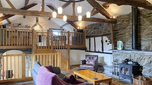A rustic interior with exposed wooden beams, a stone wall, a fireplace, and a cozy seating area with a sofa and armchair. - 2 bedroom accommodation in Satterthwaite, near Coniston (Satterthwaite, near Coniston)