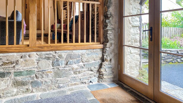 A rustic interior with a stone wall, wooden railing, and a door leading to an outdoor area. - 2 bedroom accommodation in Satterthwaite, near Coniston (Satterthwaite, near Coniston)