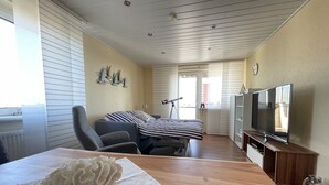 Una habitación con una mesa de madera, una silla, una cama con ropa de cama a rayas, un televisor y vistas al exterior a través de una puerta.