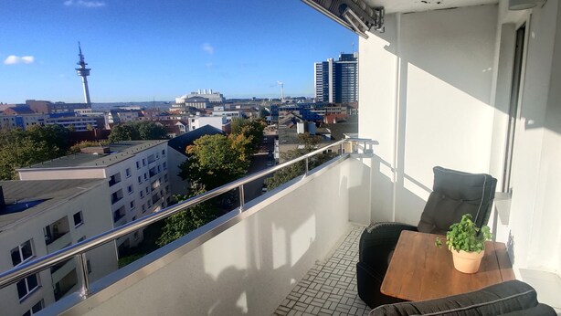 Un balcón con vista a un paisaje urbano, que incluye una torre y varios edificios.