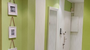 Un pasillo con paredes verdes, piso de madera y un espejo en la pared.