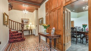 A spacious foyer with a patterned tile floor, a wooden staircase, a reception desk, and a dining area with wooden furniture.