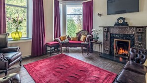 A cozy living room with a fireplace, comfortable seating, and large windows with curtains.