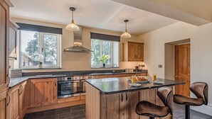 A modern kitchen with wooden cabinets, a central island, bar stools, and pendant lighting.
