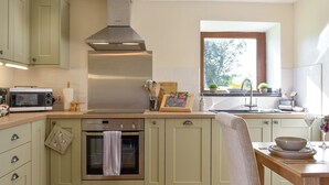 A kitchen with a built-in oven, microwave, and stainless steel range hood. There is a window providing natural light and a view of greenery outside. - 1 bedroom accommodation in Newton Le Willows (Newton Le Willows)