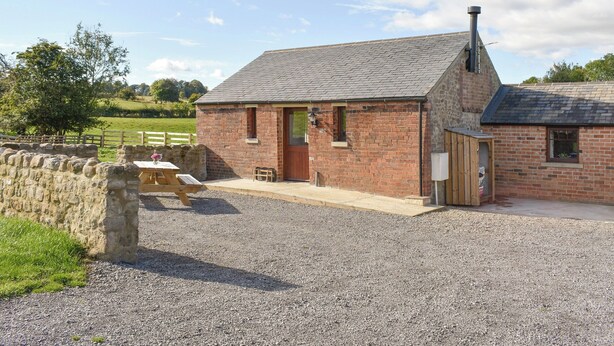 A brick building with a sloped roof, a wooden door, and a gravel driveway. - 1 bedroom accommodation in Newton Le Willows (Newton Le Willows)