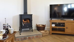 A cozy living room with a wood-burning stove, a television, and a coffee table with pastries. - 1 bedroom accommodation in Newton Le Willows (Newton Le Willows)