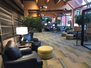 Eine moderne Lobby mit Ledersitzmöbeln, einem gemusterten Teppich und großen Fenstern mit Blick ins Freie.