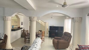 Uma sala de estar espaçosa com uma mesa de jantar, cadeiras, um sofá e uma televisão.