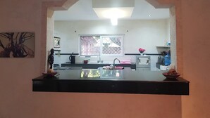 Cozinha com bancada preta, janela com grade de metal e relógio fixado na parede.