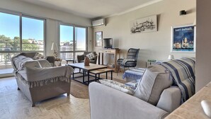 A spacious living room with a large window, a television, and a balcony.