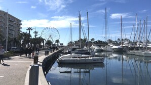 A marina with several sailboats docked, a Ferris wheel in the background, and a pedestrian walkway alongside the water.