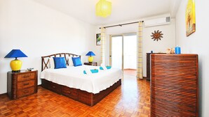 Une chambre à coucher avec un lit en bois, deux tables de chevet avec des lampes, un radiateur et une vue sur l’extérieur.