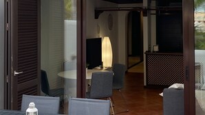 Een open terras met een tafel, stoelen, een lamp en uitzicht op het interieur door glazen deuren.