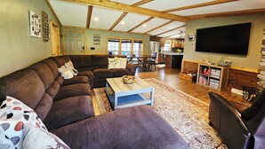 A spacious living room with a large sectional sofa, a coffee table, and a flat-screen TV mounted on the wall.