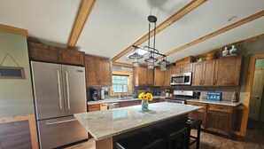 A kitchen with wooden cabinets, a stainless steel refrigerator, a granite countertop, and a central island with bar stools.