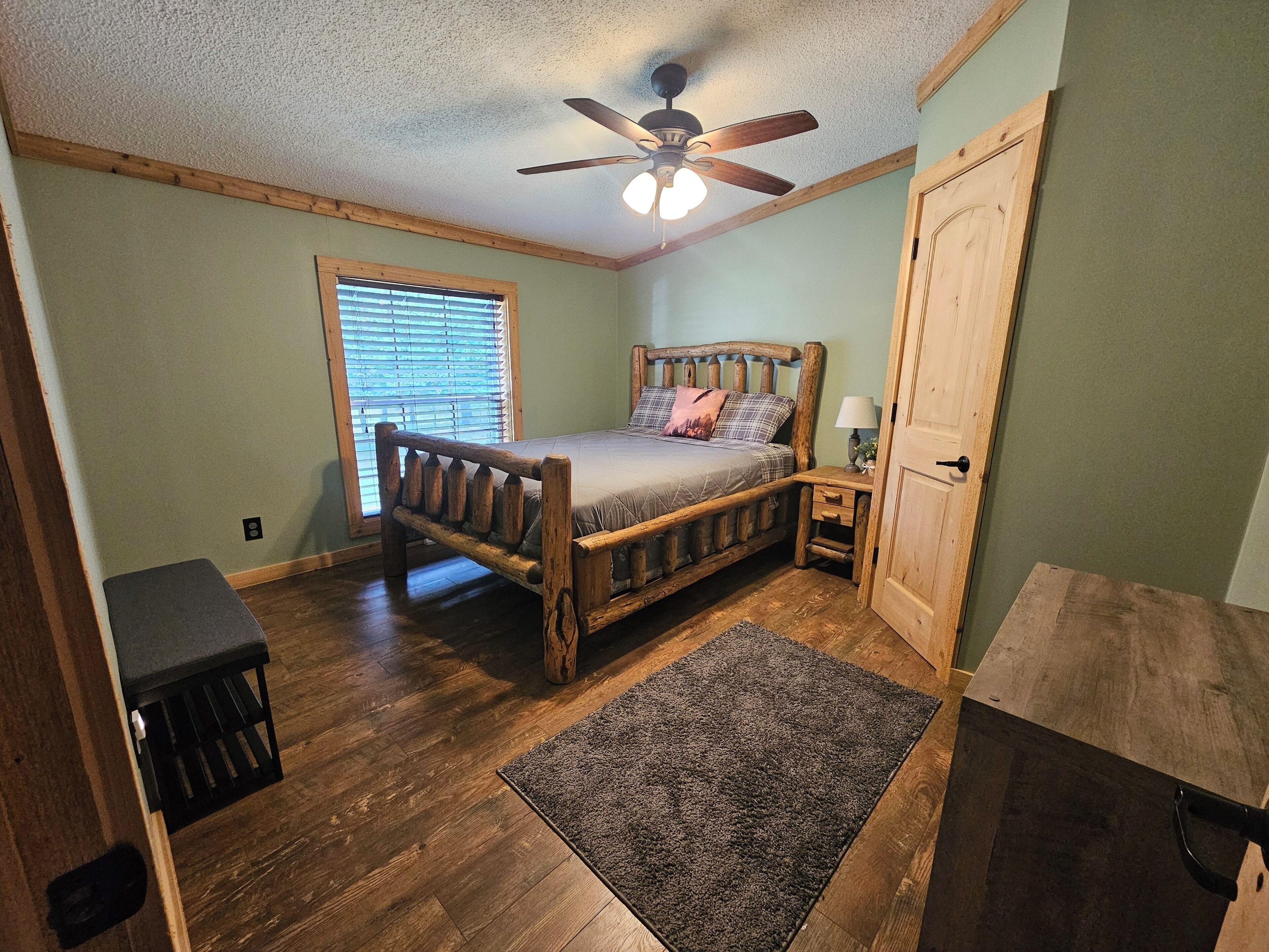 A bedroom with a wooden bed, a ceiling fan, a window with blinds, and a door.
