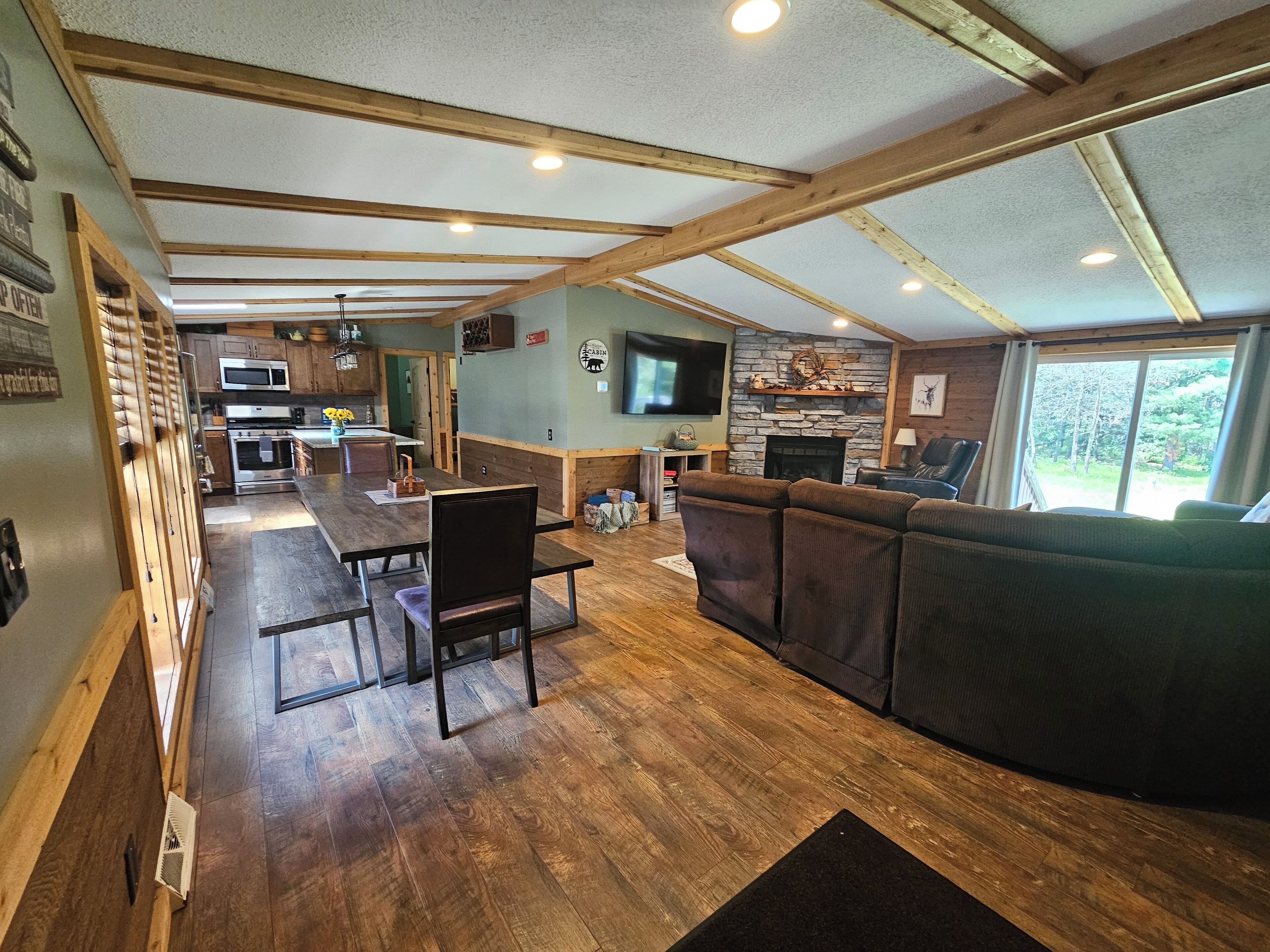 A spacious living area with a wooden ceiling, a stone fireplace, a large TV, and a couch.